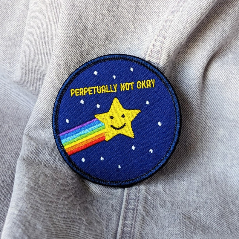 funny embroidered patch featuring a star with a rainbow trailing behind it and the words "perpetually not okay"