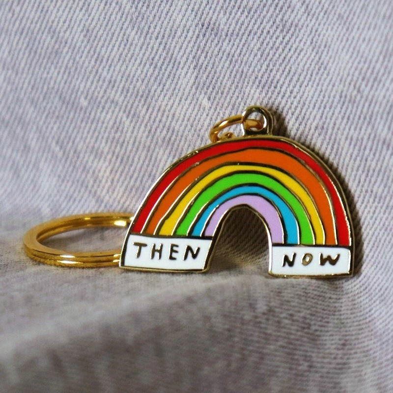 enamel keychain with a rainbow stretching between the words "then" and "now"