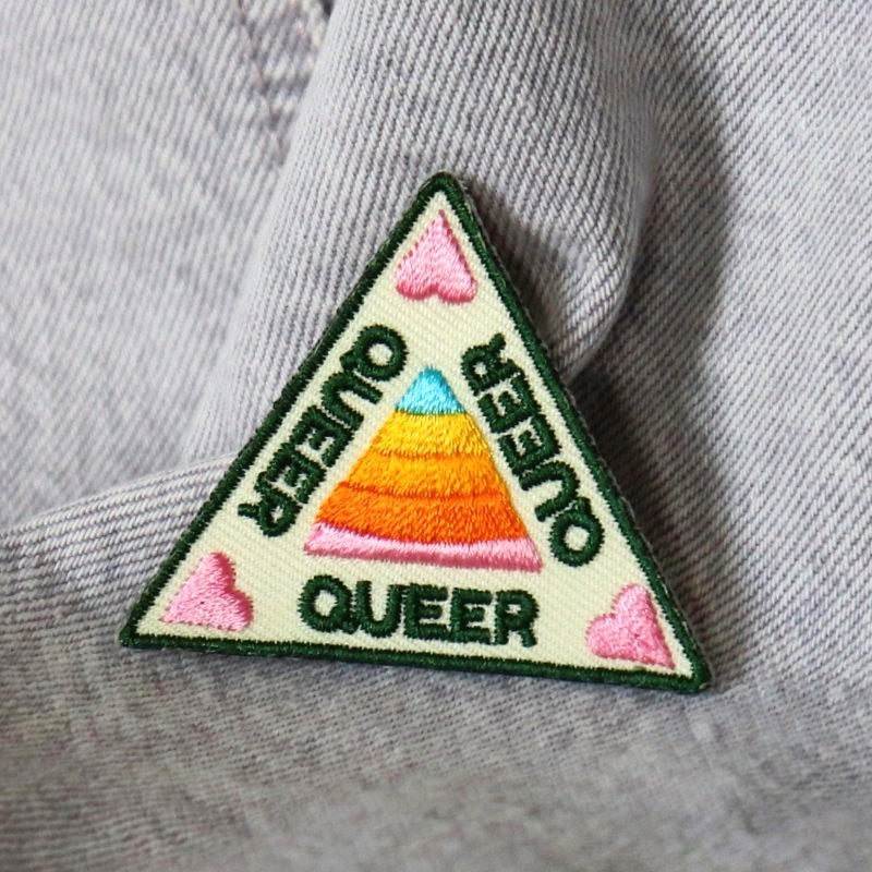 triangular patch with hearts and the word "queer" three times