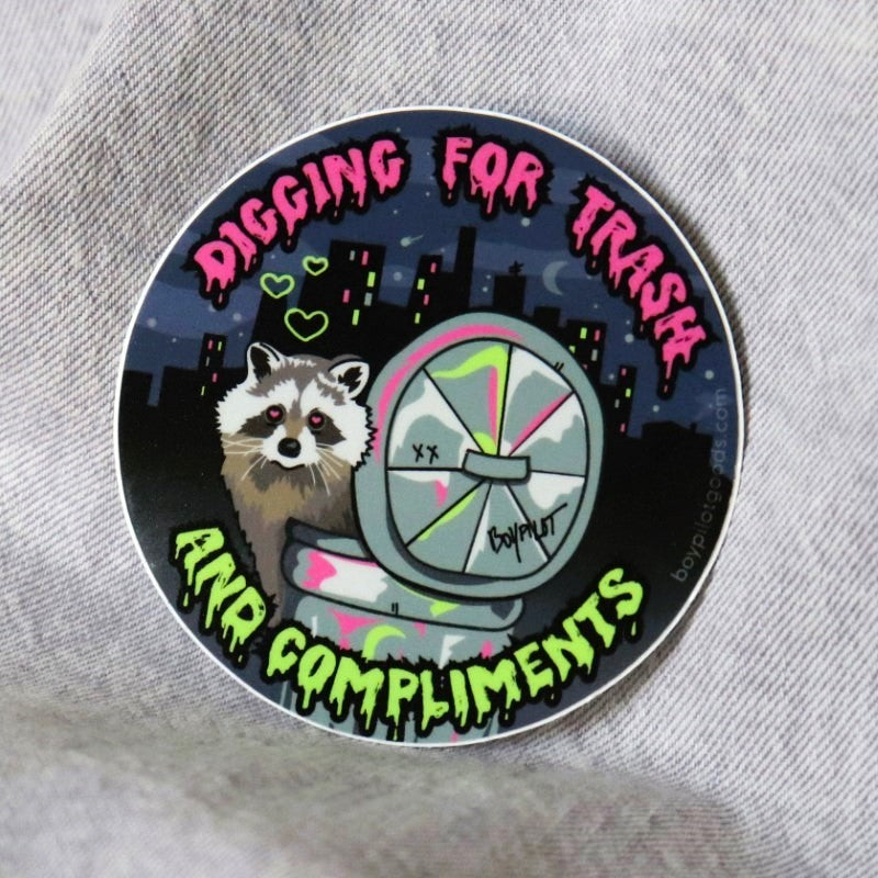 funny sticker of a raccoon in a trash can and the words "digging for trash and compliments"