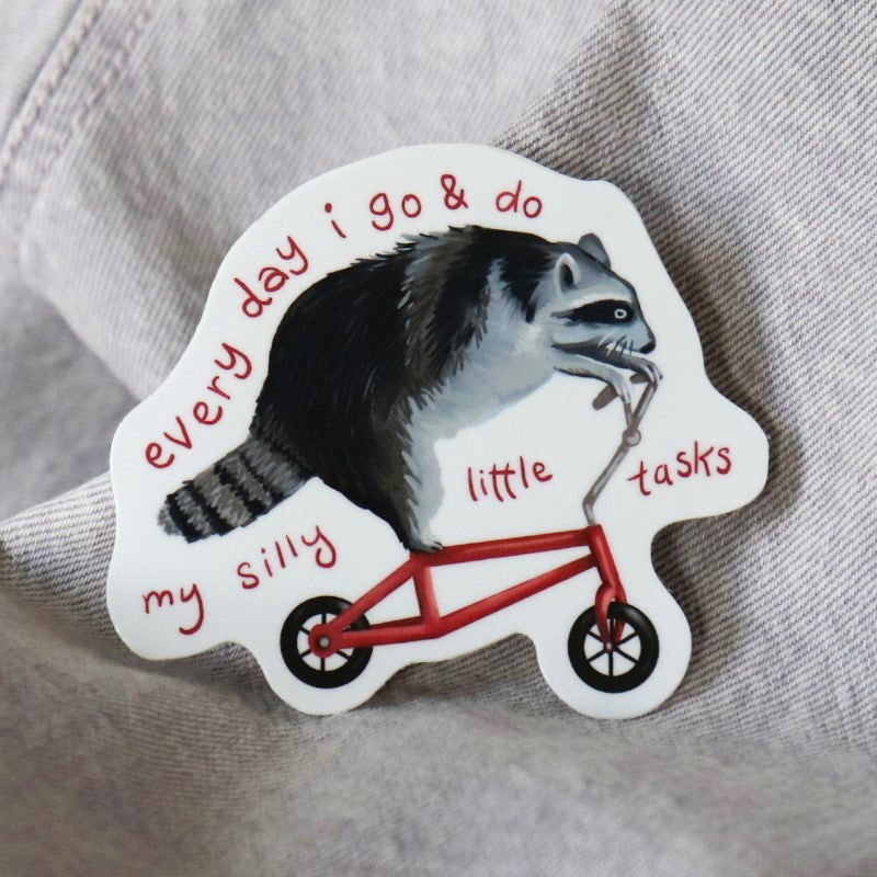 funny sticker of a raccoon riding a bike and the words "every day i go and do my silly little tasks"