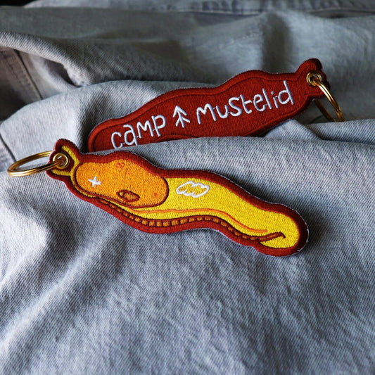 cool embroidered keychain featuring a banana slug and the words "camp mustelid" on the back