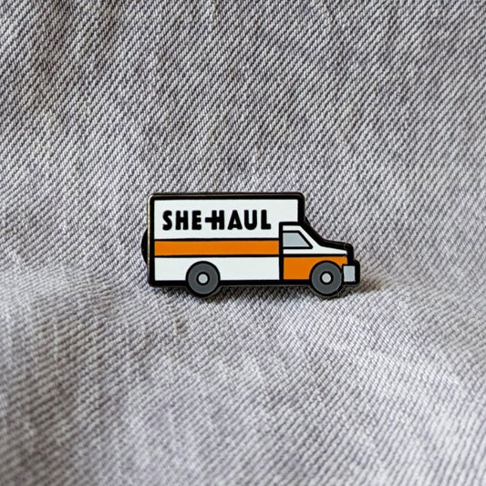 funny enamel pin of a moving truck that says "she-haul" on it