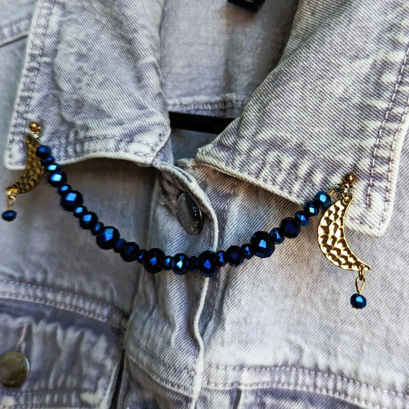 lapel pins with gold moons, and a string of blue beads between them. the moons face outward.