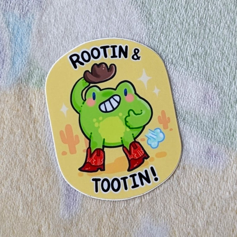 cute sticker of a cowboy frog tooting, and the words "rootin & tootin!"