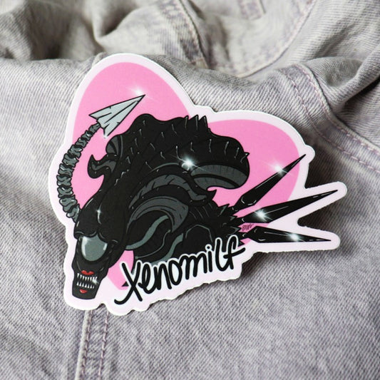 funny sticker of a scary alien wearing lipstick and the word "xenomilf"