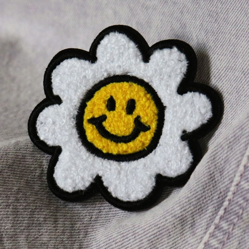 a chenille iron-on patch of a daisy with a smiley face