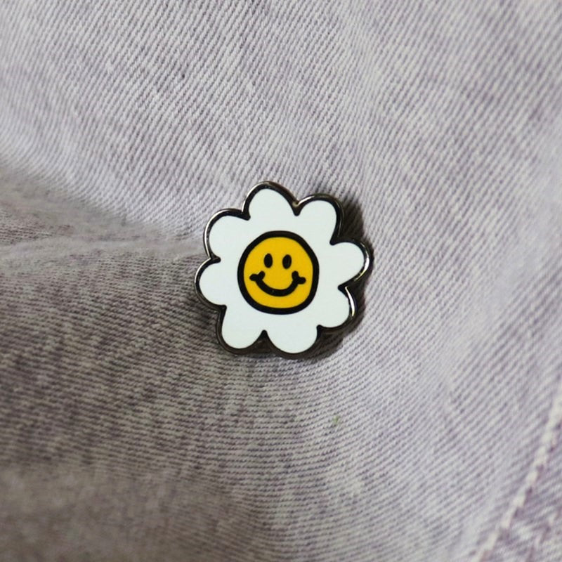 a small enamel pin of a daisy with a smiley face