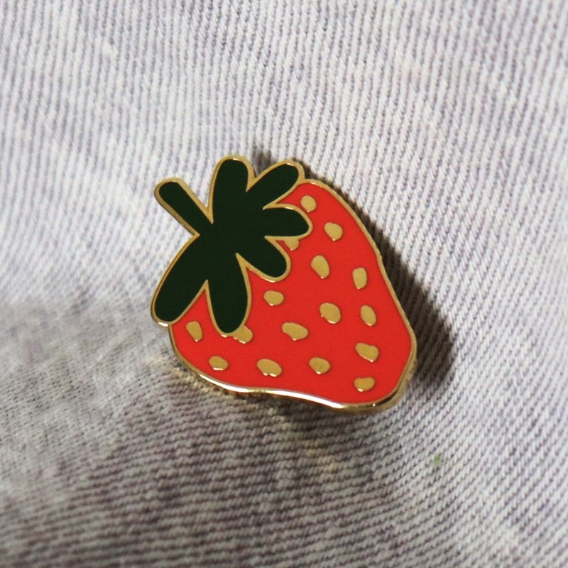 a small strawberry enamel pin